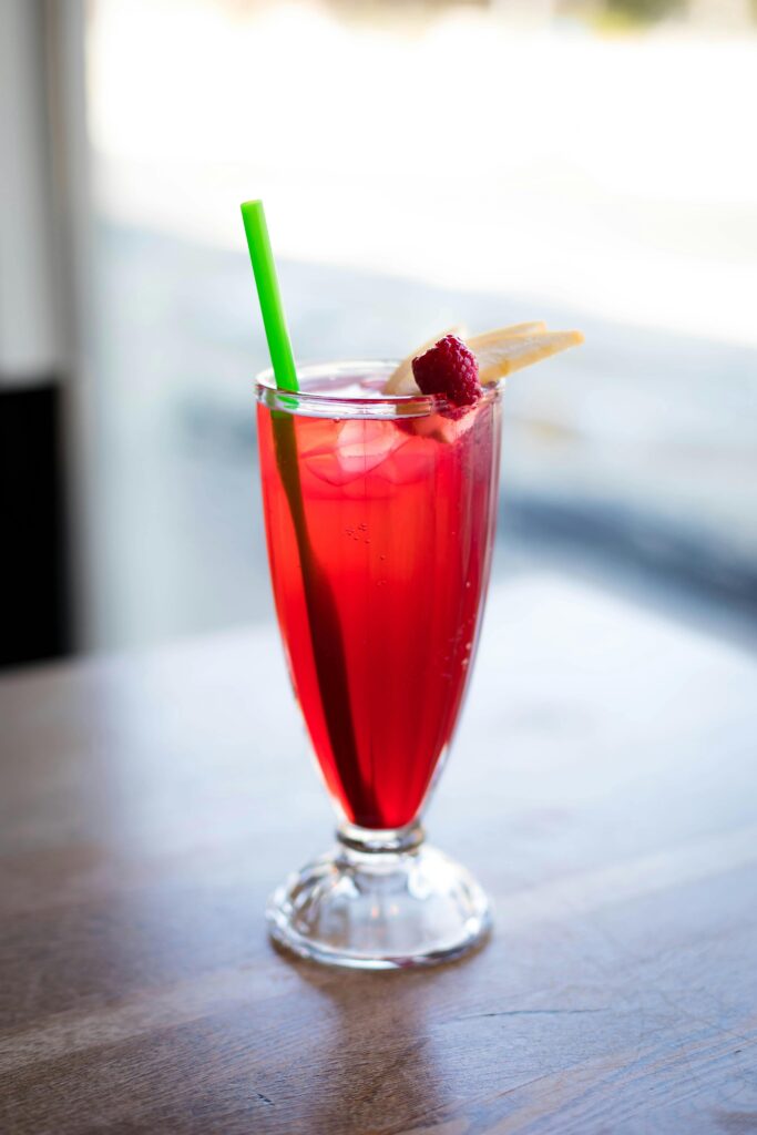 Bright red raspberry tonic in a tall glass with green straw, perfect for summer refreshment.